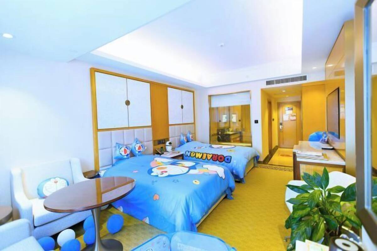 A hotel room with two beds, a small table, a sofa, and a potted plant.