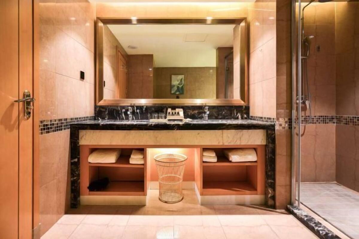 A bathroom with a marble countertop, a large mirror, a shower, and a towel rack.