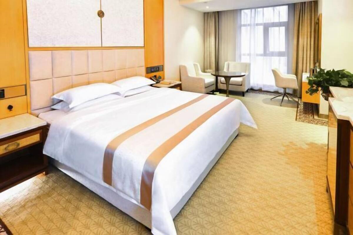 A hotel room with a large bed, a desk, two chairs, and a small table.