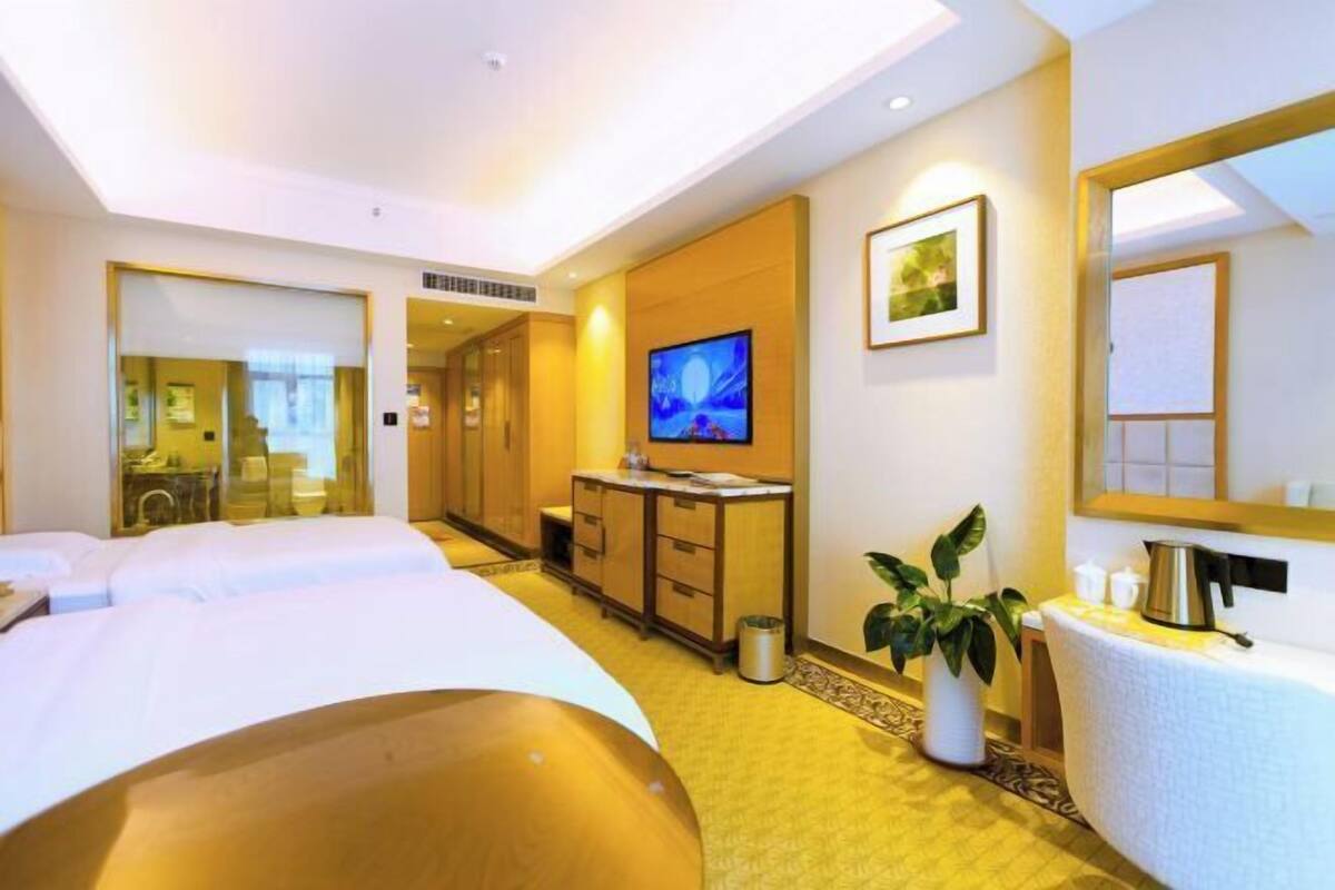 A hotel room with a large bed, a desk with a computer, a TV, and a plant.