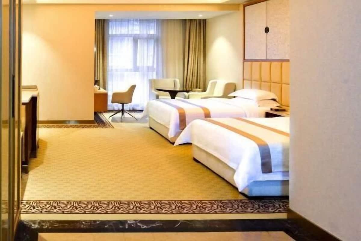 A hotel room with two beds, a desk, a chair, and a large window with curtains.