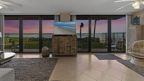 A spacious living room with a large sliding glass door leading to a balcony with a view of the beach and sunset. - Direct Oceanfront, Ground-Floor Condo Just Steps from Pool & Beach Access! (New Smyrna Beach)