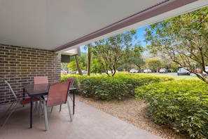 Un espace extérieur aménagé en patio, avec un mur en briques, une table en verre et des chaises rouges.