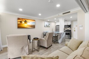 A modern living room with a sofa, armchairs, a coffee table, and a TV. There is a kitchen area with a microwave and oven in the background. - MUIRFIELD 2820 AT INNISBROOK AVAILABLE FOR THE 2027 VALSPAR PGA TOURNAMENT (Palm Harbor)