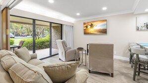 A modern living room with a sofa, armchairs, a dining table with chairs, a side table, and a large window with a view of the outdoors. - MUIRFIELD 2820 AT INNISBROOK AVAILABLE FOR THE 2027 VALSPAR PGA TOURNAMENT (Palm Harbor)