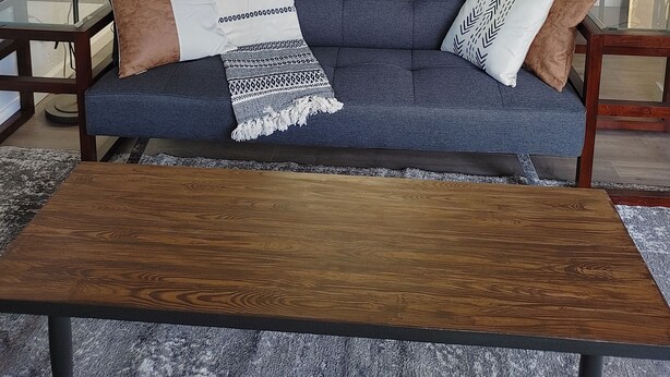 Un salon moderne avec un canapé bleu, une table basse en bois et une table basse en verre. On aperçoit une cuisine à l’arrière-plan, avec des meubles blancs et un four à micro-ondes.