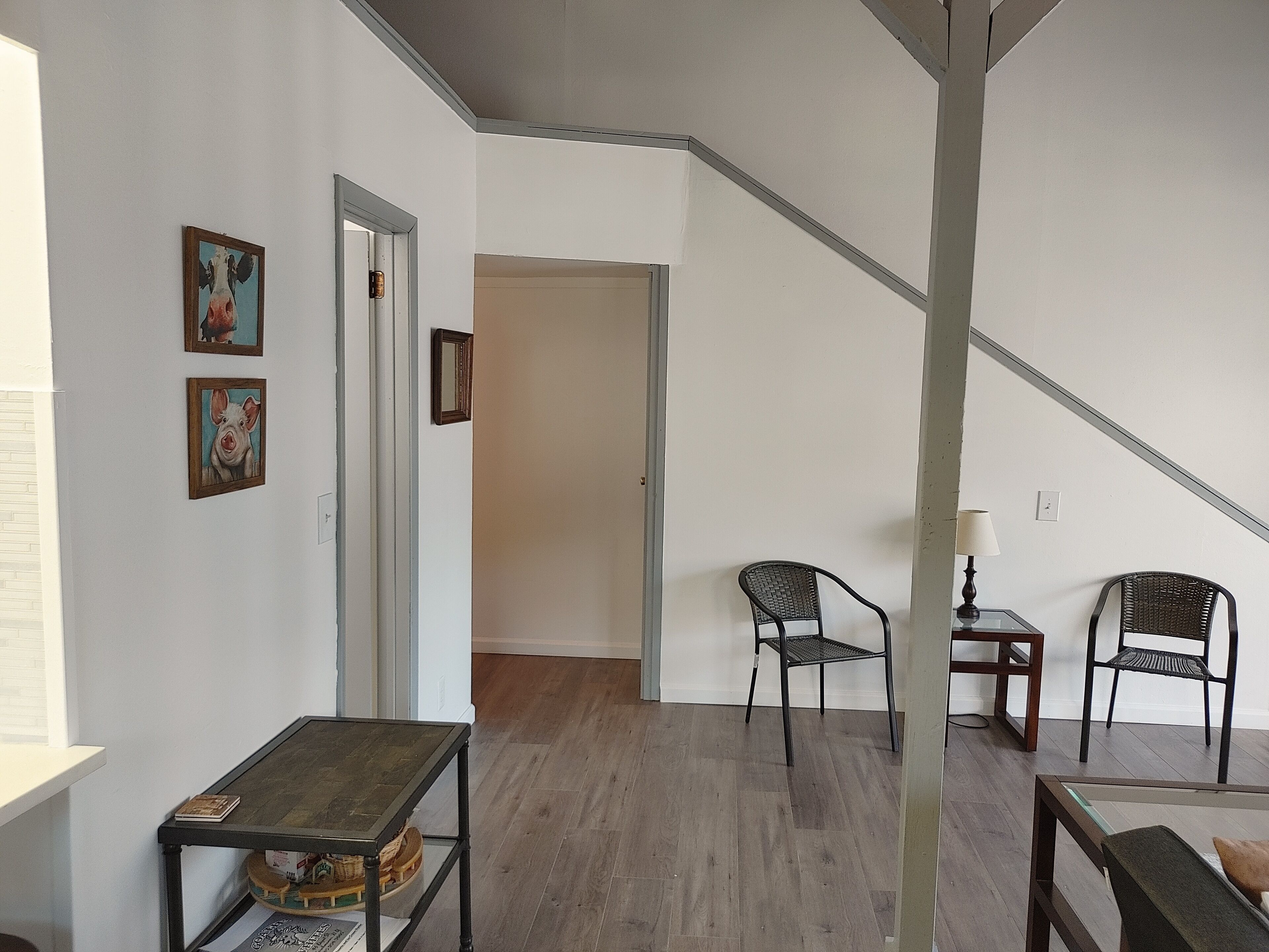 Ein Zimmer mit Holzboden, einem kleinen Tisch mit Lampe, zwei Stühlen und einer Treppe.