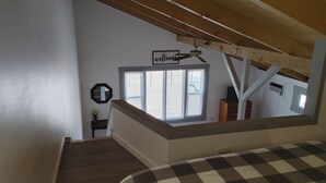 Une chambre avec une couvre-lit à carreaux, une fenêtre avec des stores, un ventilateur de plafond et un panneau d’accueil.