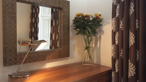 A mirror with a checkered frame, a desk lamp, and a vase with flowers on a wooden surface. - Luxury central Edinburgh with stunning views of castle! (Edinburgh)