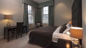 A hotel room with a bed, a desk, a chair, and a view of buildings through large windows. - Luxury central Edinburgh with stunning views of castle! (Edinburgh)