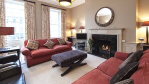 A living room with a red sofa, a black ottoman, a fireplace, and a television. - Luxury central Edinburgh with stunning views of castle! (Edinburgh)