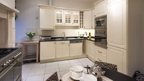 A modern kitchen with white cabinets, a black countertop, stainless steel appliances, and a dining area with a tray of cups and a teapot. - Luxury central Edinburgh with stunning views of castle! (Edinburgh)
