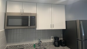 Una cocina con armarios blancos, microondas de acero inoxidable, cafetera y tostadora.