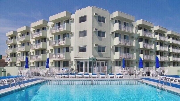 Un hotel de varios pisos con piscina, balcones y sillones de descanso.