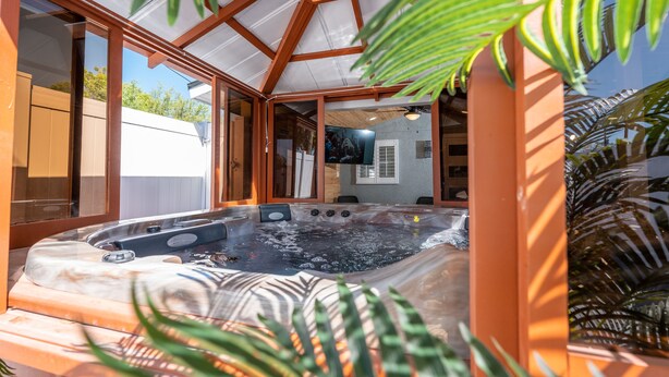 Un jacuzzi con estructura de madera y paredes de vidrio, rodeado de plantas en macetas.