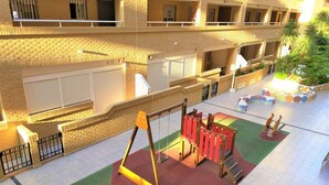 A multi-level building with a children's play area on the ground floor, featuring swings and a climbing structure. - ACV - Neptuno-2ª Línea Planta 6 Norte (Oropesa del Mar)