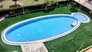 A swimming pool with a Mickey Mouse design, surrounded by a green lawn and umbrellas. - ACV - Neptuno-2ª Línea Planta 6 Norte (Oropesa del Mar)