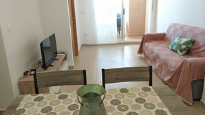 A living room with a television, a green bucket, a sofa with a patterned cover, and a patterned rug. - ACV - Neptuno-2ª Línea Planta 6 Norte (Oropesa del Mar)