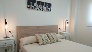 A neatly arranged bedroom with a wooden headboard, two bedside tables with lamps, and a decorative wall piece above the bed. - ACV - Neptuno-2ª Línea Planta 6 Norte (Oropesa del Mar)