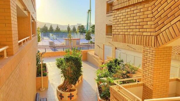 A courtyard with brick walls, potted plants, and a view of a tennis court in the background. - ACV - Neptuno-2ª Línea Planta 6 Norte (Oropesa del Mar)