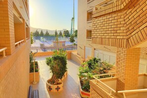 Une cour intérieure avec des murs en briques, des plantes en pot et, au fond, une vue sur un court de tennis.