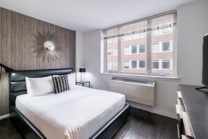 Une chambre d’hôtel moderne avec un grand lit, un miroir fixé au mur, une fenêtre avec des stores et un radiateur.