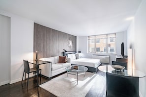 Un salon moderne avec une table basse en verre, un canapé, un fauteuil et une grande fenêtre.