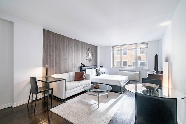 A modern living room with a glass coffee table, a sofa, a chair, and a large window.