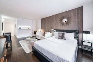 A modern hotel room with a large bed, a sofa, a desk, and a mirror on the wall.