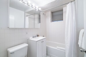 A bathroom with a toilet, sink, mirror, and bathtub.