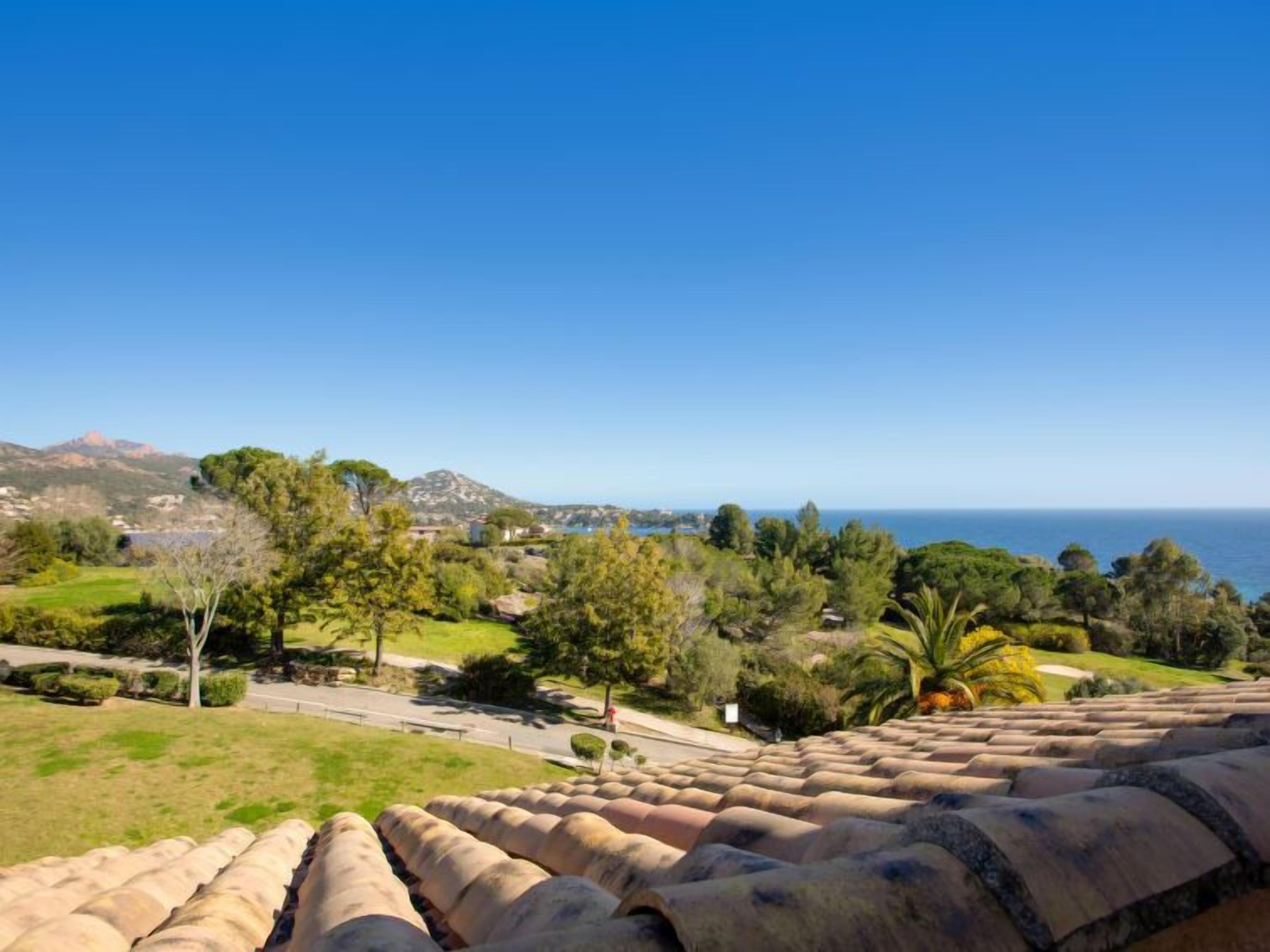 Vista costeira a partir de um telhado de terracota, com vista para uma paisagem verdejante com árvores e um céu azul límpido.