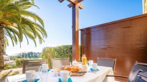 An outdoor dining area with a table set for breakfast, including bread, juice, and cups. - Le Village (C4 010) by Interhome (Agay Village Cap Esterel)