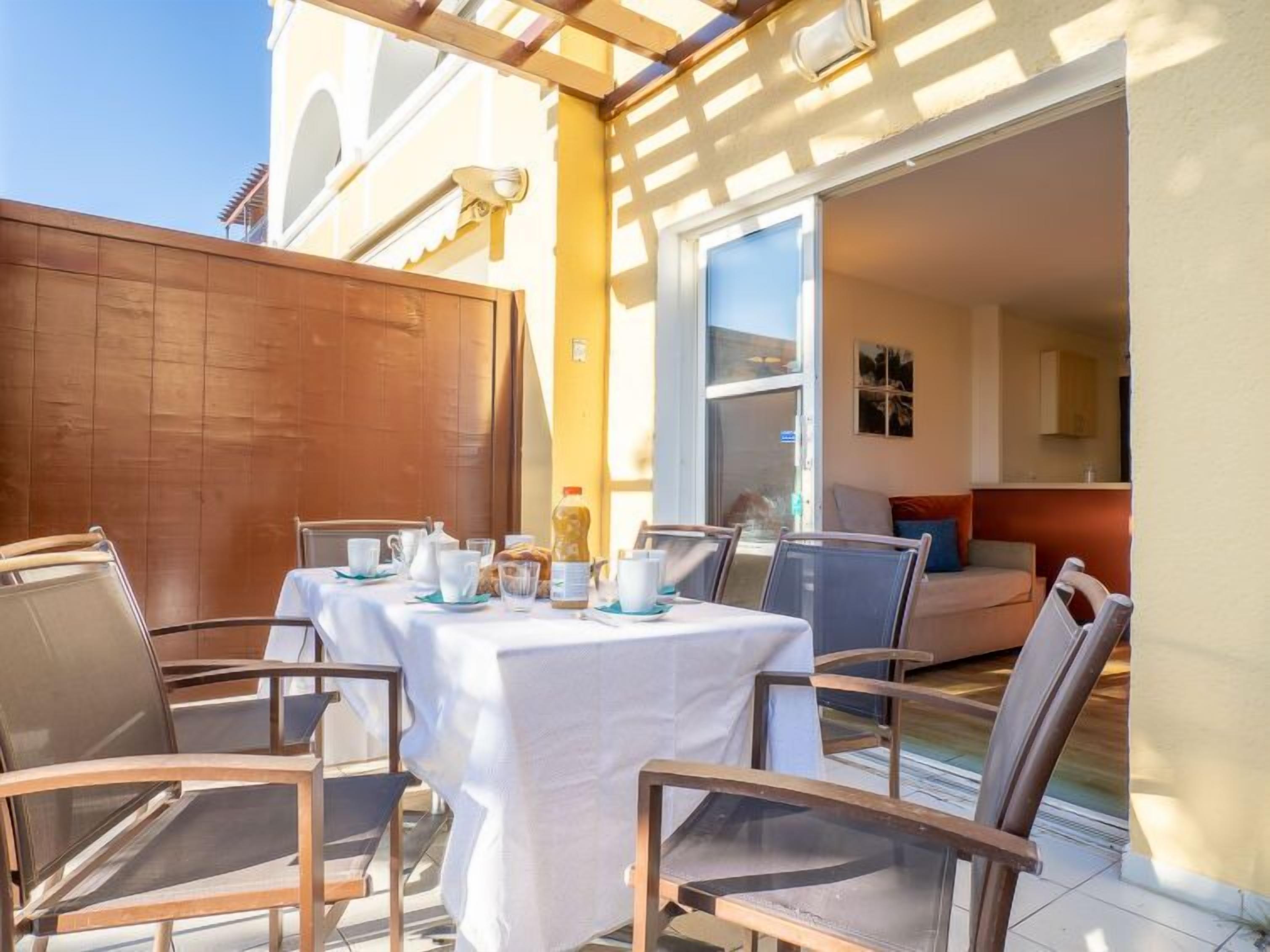 Un patio con mesa lista para comer, sillas y cerramiento de madera.