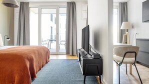 Et hotelværelse med seng, fjernsyn, skrivebord og stol. Der er en balkon med bord og stole udenfor.