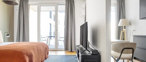 Ett hotellrum med en säng, en tv, ett skrivbord och en stol. Det finns en balkong med ett bord och stolar utanför.