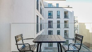 En balkon med et bord og to stole, med udsigt over en moderne bygning med flere vinduer og balkoner.