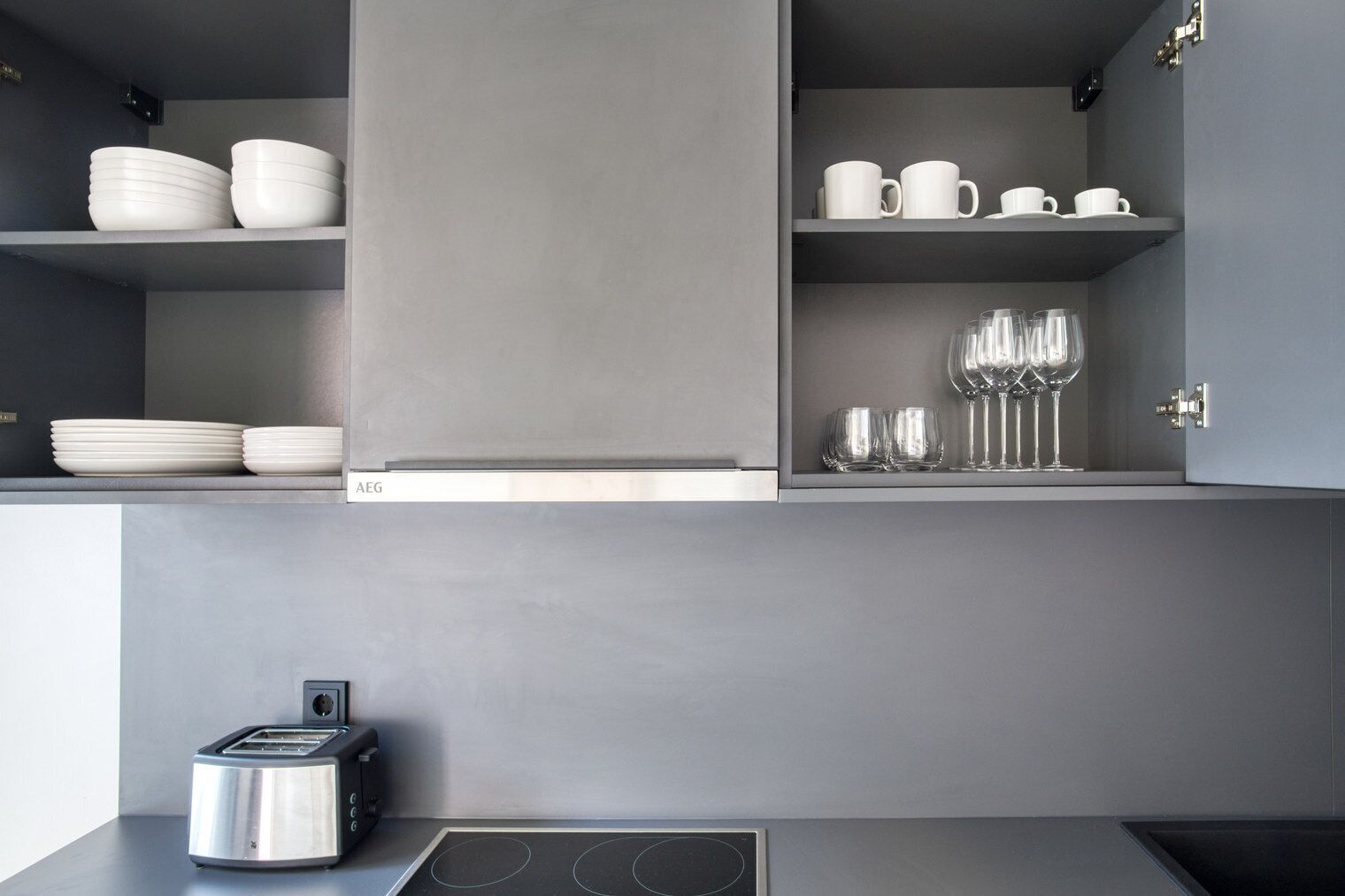 Une cuisine moderne avec des meubles de couleur grise, un grille-pain encastré et des étagères où sont rangées de la vaisselle et des verres blancs.