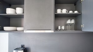 Et moderne køkken med grå skabe, en indbygget toaster og hylder med hvide tallerkener og glas.