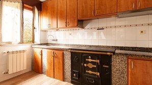 A kitchen with wooden cabinets, a granite countertop, a stove, and a window with curtains. - Casina de Cuevas - country house in Cuevas del Agua (Ribadesella) (Nocedo (Cuevas Del Agua))