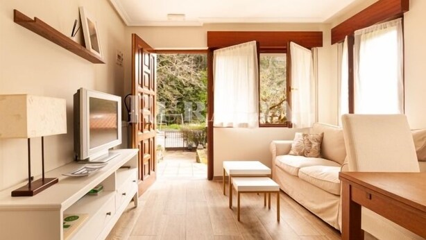 A living room with a sofa, TV, and a small table. There is a window with curtains and a view of greenery outside. - Casina de Cuevas - country house in Cuevas del Agua (Ribadesella) (Nocedo (Cuevas Del Agua))
