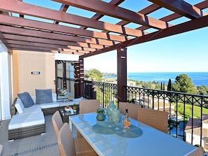 A balcony with wicker furniture, a glass table, and a view of the sea.