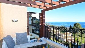 A balcony with a view of the sea, a sofa with cushions, a small table with fruits, and a book. - Le Village (C4 323) by Interhome (Agay Village Cap Esterel)