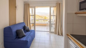 Une pièce avec un canapé bleu, un téléviseur et un balcon donnant sur la campagne.