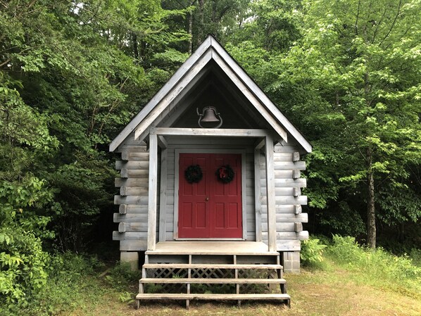 Une cabane en bois avec une porte rouge, une cloche au-dessus de la porte et une guirlande de chaque côté.