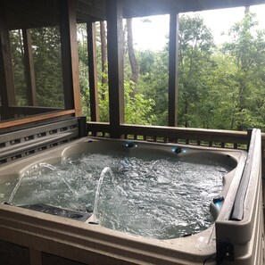 Un bain à remous avec jets d’eau, entouré de poutres en bois et offrant une vue sur une forêt.