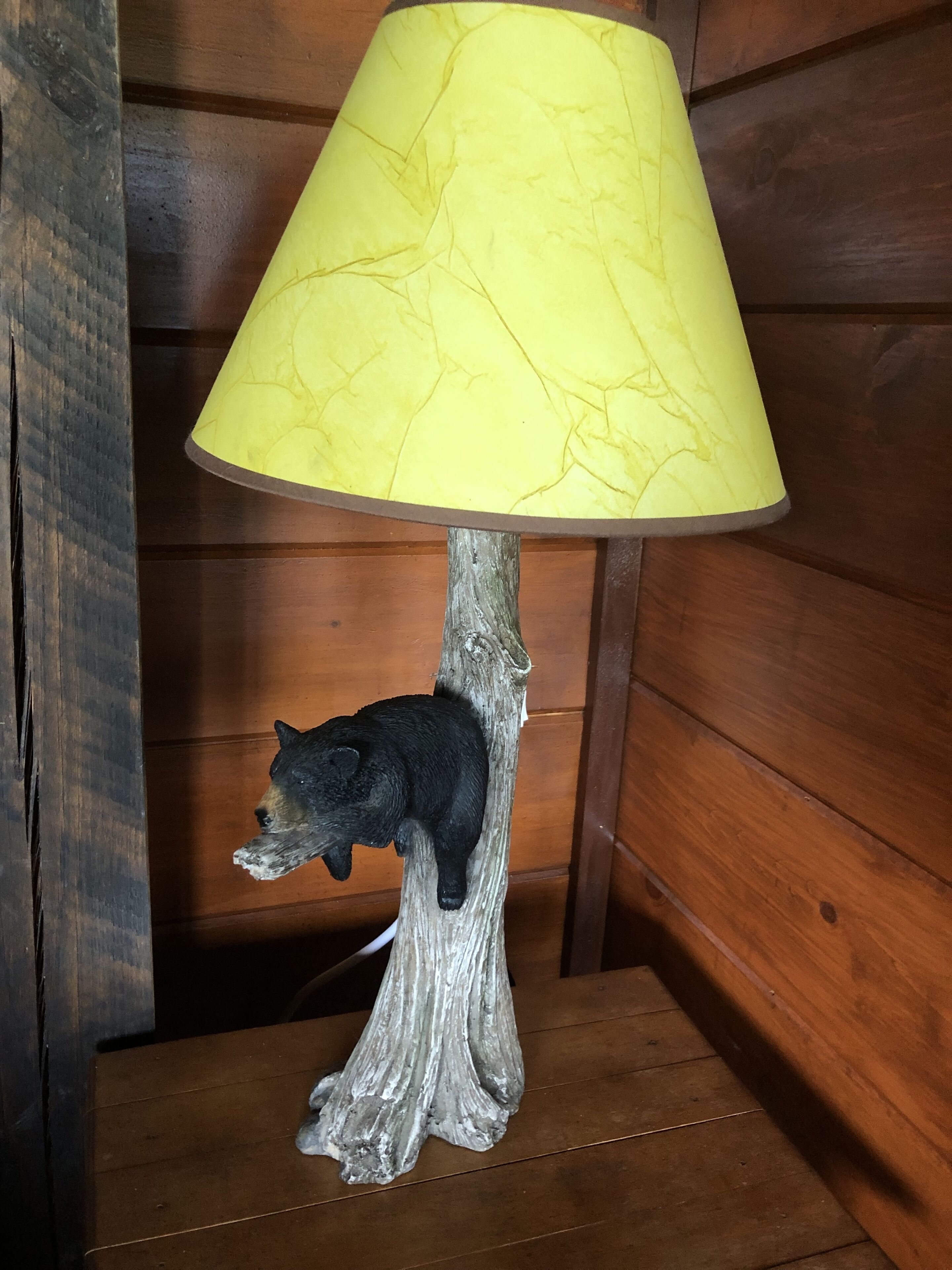 A lamp with a bear figurine on its base, set against a wooden wall.