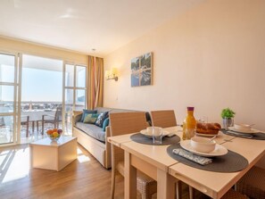 A modern living room with a sofa, dining table, and a balcony with a view. - L'Esquinade (H4 233) by Interhome (Agay Village Cap Esterel)