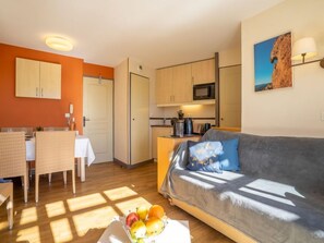 A cozy living room with a sofa, a dining area with a table and chairs, and a kitchen with cabinets and appliances.