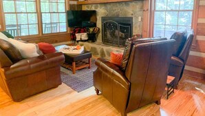 A cozy living room with a stone fireplace, leather sofas, and a television. - Cozy Cabin in woods with Hot Tub, Porch Swing Bed and Fire Pit in Aska Adventure (Blue Ridge)