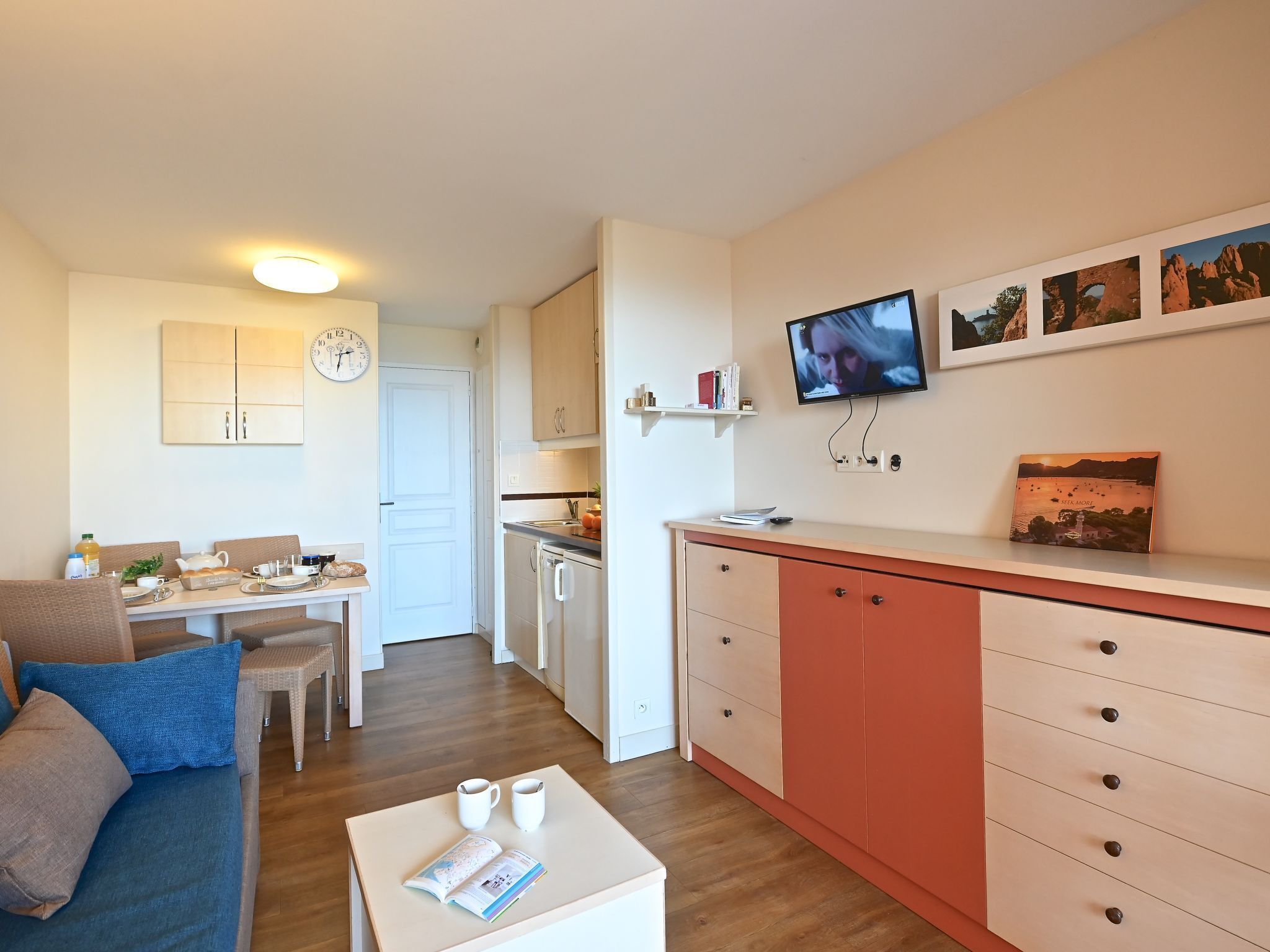 Een moderne keuken met een televisie, kastjes en een eethoek met een tafel en stoelen.